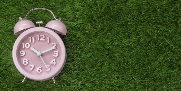 Çalar saat yeşil çimenlerin üzerinde pembe, yakın çekim