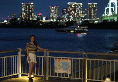 Tokyo, Japonya - 15 Ağustos 2018. Kadın turist resimleri Odaiba, Tokyo cityscape güzel manzara ile akşam plaj için poz.