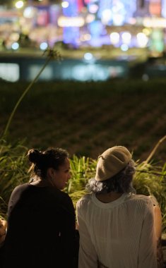 Tokyo, Japonya - 15 Ağustos 2018. Arkadan görünüşü birlikte ışıklar bokeh arka planda ile sokak kaldırım kenarında oturan arkadaşlar
