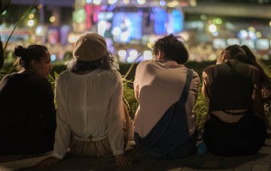 Tokyo, Japonya - 15 Ağustos 2018. Arkadan görünüşü birlikte ışıklar bokeh arka planda ile sokak kaldırım kenarında oturan arkadaşlar