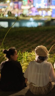 Tokyo, Japonya - 15 Ağustos 2018. Arkadan görünüşü birlikte ışıklar bokeh arka planda ile sokak kaldırım kenarında oturan arkadaşlar
