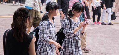 Tokyo, Japonya - 19 Ağustos 2018. Japon kızlar Shibuya sokakta smartphone ile aynı elbise.