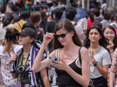 Tokyo, Japonya - 19 Ağustos 2018. Kadın turist ile karşıya Shibuya içinde smartphone.