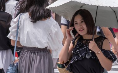 Tokyo, Japonya - 19 Ağustos 2018. Smartphone ve Shibuya içinde karşıdan karşıya bekleyen şemsiye ile Japon kız.