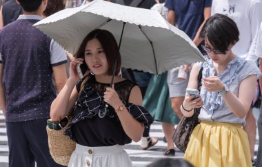 Tokyo, Japonya - 19 Ağustos 2018. Smartphone ve Shibuya içinde karşıdan karşıya bekleyen şemsiye ile Japon kız.
