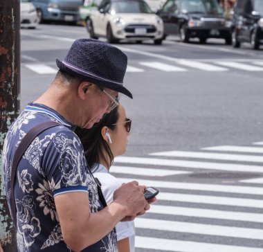 Tokyo, Japonya - 19 Ağustos 2018. Shibuya içinde karşıdan karşıya bekleyen smartphone ile bir şapka giyen Japon eman.