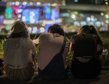 Tokyo, Japonya - 15 Ağustos 2018. Arkadan görünüşü birlikte ışıklar bokeh arka planda ile sokak kaldırım kenarında oturan arkadaşlar