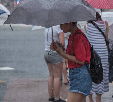 Tokyo, Japonya - 29 Temmuz 2018. Shibuya içinde yağmurlu tayfun sezonunda bir şemsiye tutan smartphone ile Japon kız.