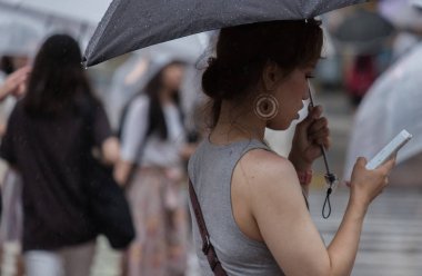 Tokyo, Japonya - 29 Temmuz 2018. Shibuya içinde yağmurlu tayfun sezonunda bir şemsiye tutan smartphone ile Japon kız.