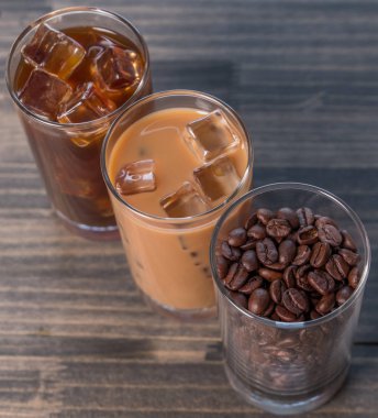 Ahşap arka plan üzerinde siyah kahve, soğuk latte ve fasulye buzlu