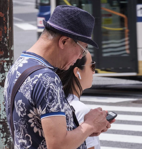 Tokyo, Japonya - 19 Ağustos 2018. Shibuya içinde karşıdan karşıya bekleyen smartphone ile bir şapka giyen Japon eman.
