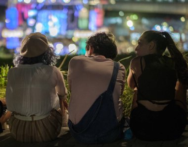 Tokyo, Japonya - 15 Ağustos 2018. Arkadan görünüşü birlikte ışıklar bokeh arka planda ile sokak kaldırım kenarında oturan arkadaşlar