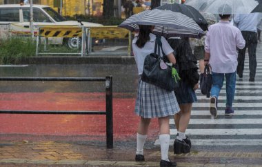 Tokyo, Japonya - 29 Temmuz 2018. Japon liseli kız yağmurlu tayfun sezonu boyunca şemsiye ile karşıya.