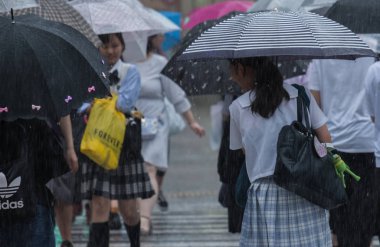 Tokyo, Japonya - 29 Temmuz 2018. Japon liseli kız yağmurlu tayfun sezonu boyunca şemsiye ile karşıya.