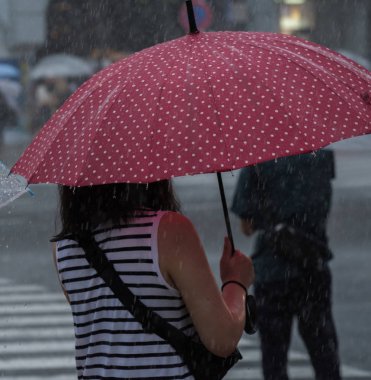 Tokyo, Japonya - 29 Temmuz 2018. Kırmızı şemsiye yağmurlu tayfun sezonu boyunca şemsiye ile karşıdan karşıya bekleyen kadınla.