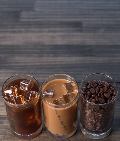 Black iced coffee, cold latte, and beans over wooden background