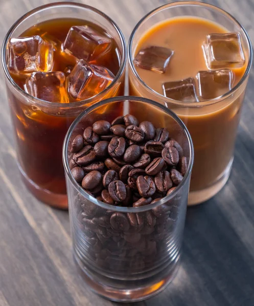 Black iced coffee, cold latte, and beans over wooden background