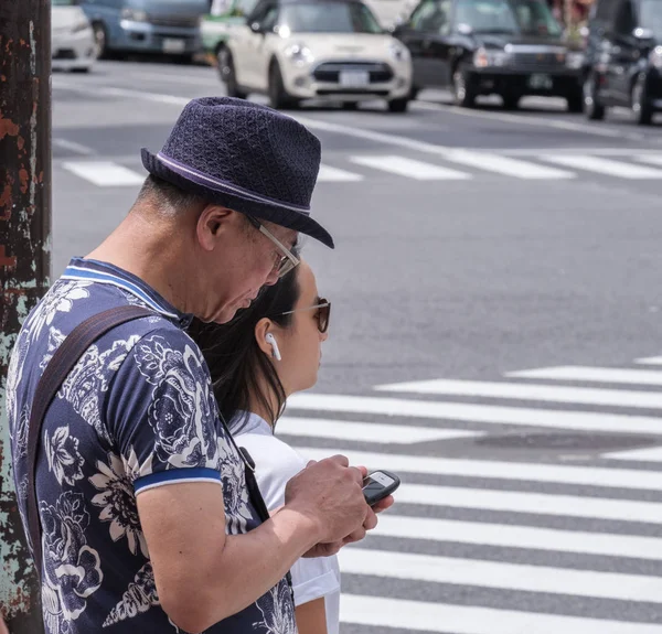 Tokyo, Japonya - 19 Ağustos 2018. Shibuya içinde karşıdan karşıya bekleyen smartphone ile bir şapka giyen Japon eman.