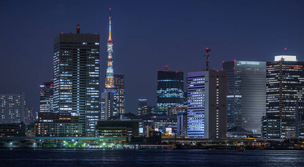 TOKYO, JAPAN - JUNE 29TH, 2019. High rise buildings in Tsukuda, Tokyo with dinner cruise houseboat (locally known as yakabutane) cruising in Sumida river in the foreground at dusk