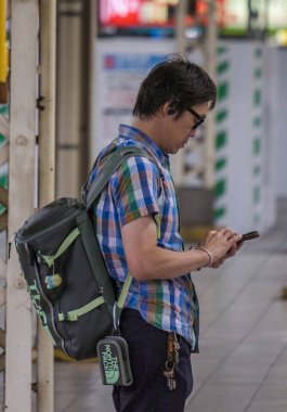 Tokyo, Japonya - 16 Eylül 2018. Erkek banliyö ile smartphone Yurakucho tren istasyonu platformu.