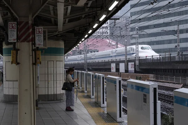2018 東京都 有楽町駅ホームに立っている女性の通勤電車バック グラウンドで通り過ぎる高速列車で到着するには — ストック写真