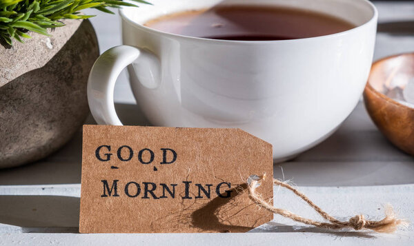 Close up view of Good morning label with cup of tea on white wooden background