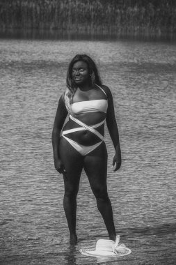 Junge dunkelhutige Frau mit langen Haaren im Bikini und Hut im Wasser in schwarz / Wei