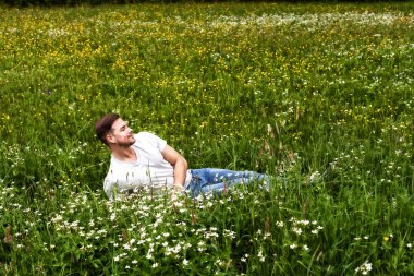 Sakallı genç adam bir dağ çayırında yatıyor ve çiçek kokusundan hoşlanıyor..