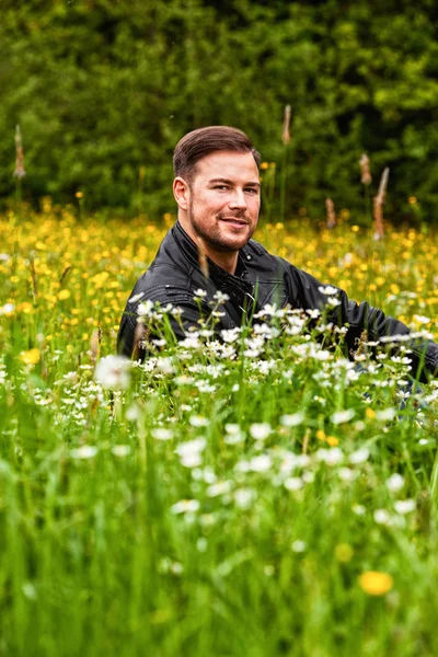 Young Man Leather Jacket Sitting Flower Meadow Looking Camera — Stock Photo, Image