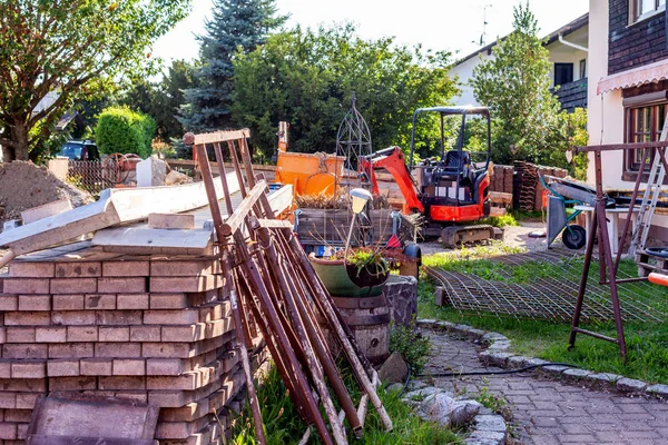 Construction sites warehouse with excavator, iron grid, paving stones, ramp and crane bucket.