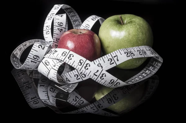 Green and red apples surrounded with measurement tape on black with reflection