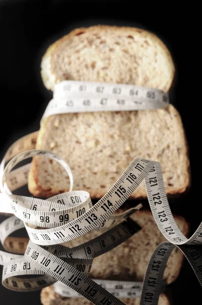 A slice of bread surrounded by a measurement tape on black with reflection