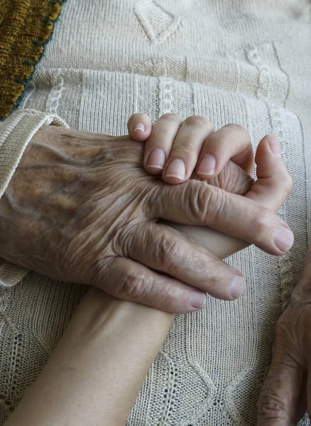 Närbild rynkig hand hållande en yngre hand — Stockfoto