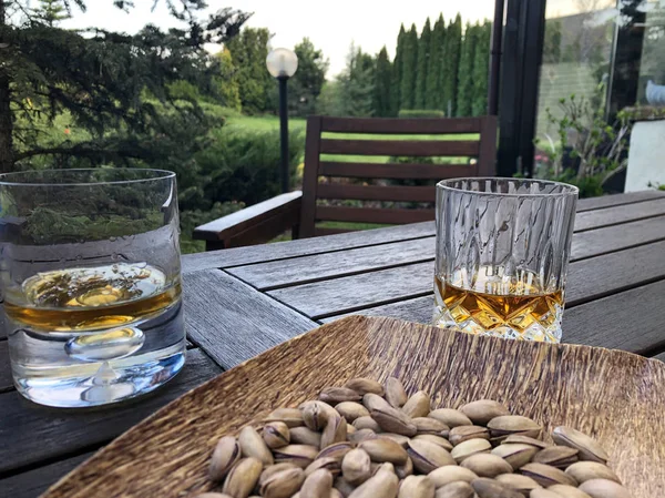 Copos de uísque e prato de frutas secas na mesa no jardim — Fotografia de Stock