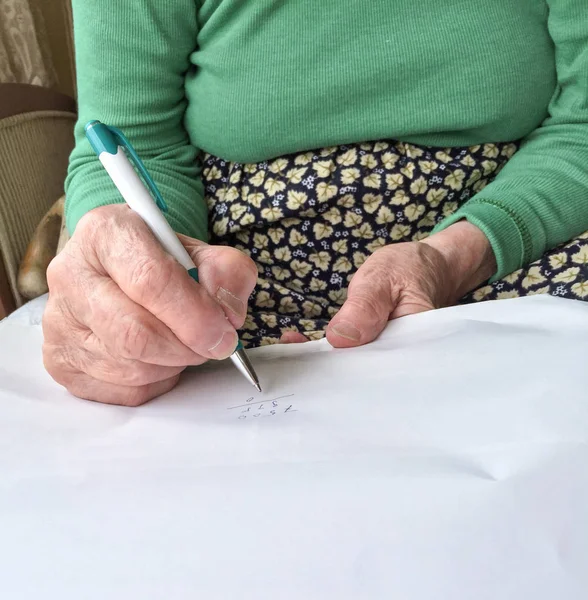 wrinkled hands of a senior woman writing on white paper