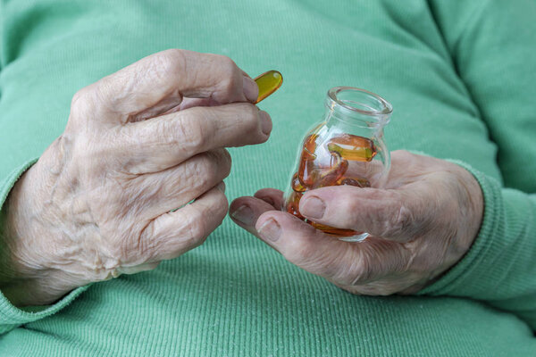 wrinkled hands of a senior person holding vitamin pills