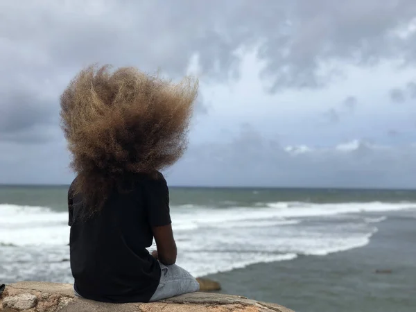 Hombre solitario con el pelo largo sentado en primera línea de playa en un día ventoso — Foto de Stock
