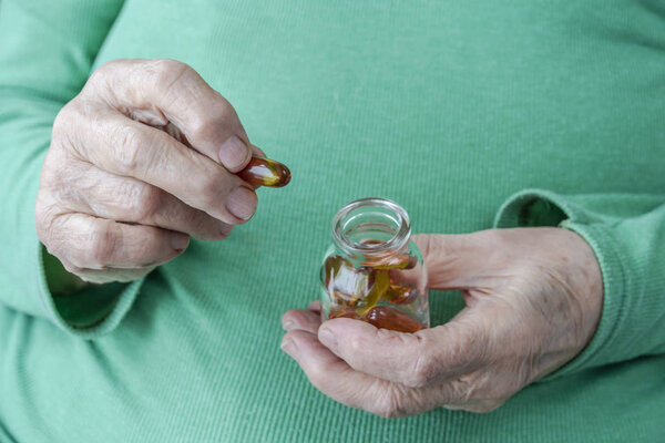 wrinkled hands of a senior person holding vitamin pills 