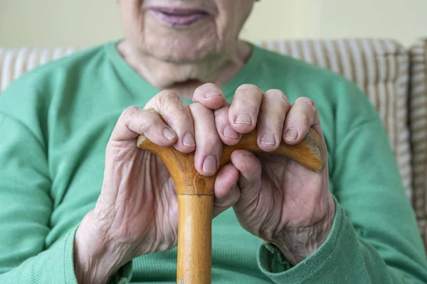 wrinkled hands of a senior person holding a walking cane