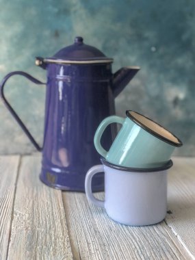 ahşap bir masa üzerinde mavi renkli emaye çaydanlık ve kupalar
