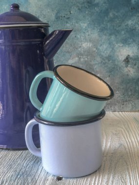 ahşap bir masa üzerinde mavi renkli emaye çaydanlık ve kupalar