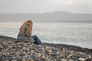 sonbaharda çakıllı bir plajda deniz de oturan kadın