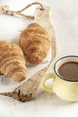 Tahta bir masada çıtır kruvasan ve bir fincan kahve.
