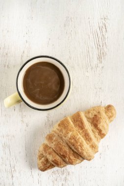 Tahta bir masada çıtır kruvasan ve bir fincan kahve.