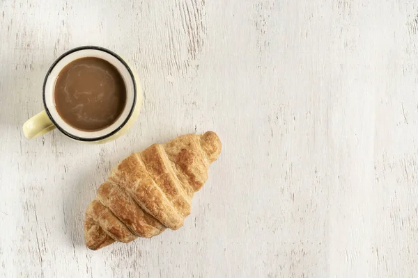 Croissant crujiente y taza de café en una mesa de madera — Foto de Stock