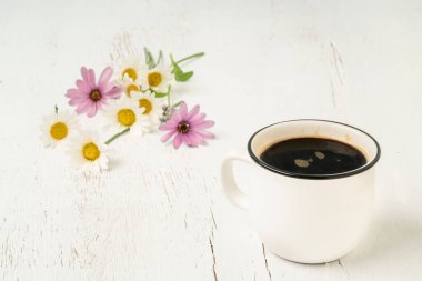 Bahar çiçekleriyle süslenmiş ahşap bir masada bir fincan Americano kahvesi.