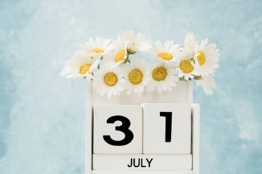 White cube calendar for july decorated with daisy flowers over blue with copy space clipart