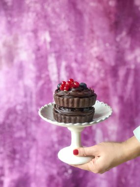 Elinde çikolatalı pastayla pembe arka planda fotokopi çeken bir kadının eli.