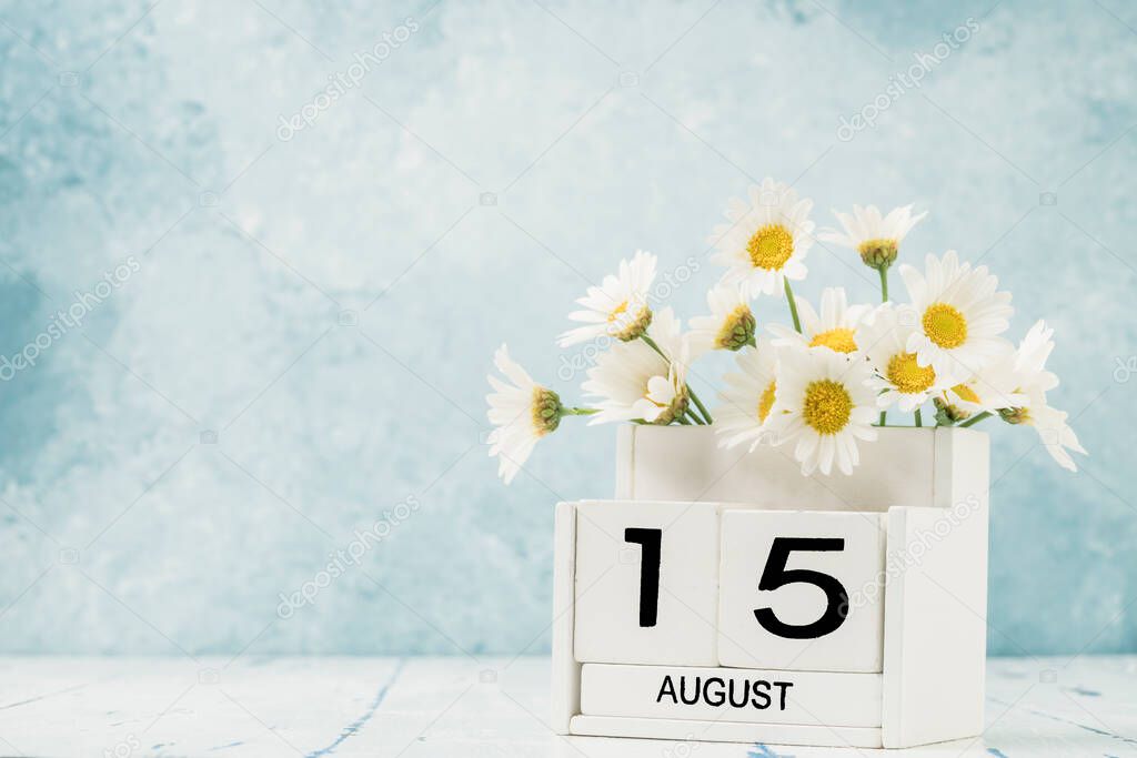 White cube calendar for august decorated with daisy flowers over blue with copy space