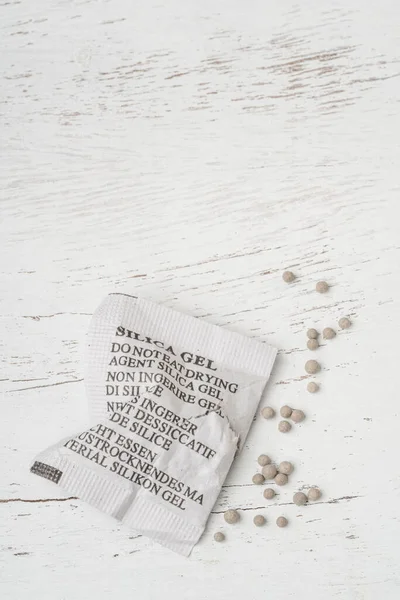 Desiccant or silica gel in white paper packaging, spread on the wooden background